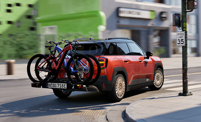 Ein orangener SUV fährt durch die Stadt, am Heck ist ein Fahrradträger mit zwei Mountainbikes montiert.