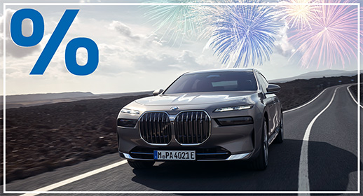 Diese Werbegrafik zeigt den luxuriösen, vollelektrischen BMW i7 in einem eleganten Dunkelgrau, der auf einer modernen Straße vor einer imposanten Bergkulisse bei einsetzender Dämmerung fährt. Das Flaggschiff der Marke ist frontal abgebildet, wodurch die beleuchtete Umrandung des großen Kühlergrills („Iconic Glow“) und die markanten, schmalen Kristallscheinwerfer besonders stark zur Geltung kommen. Die Szenerie wirkt durch die kargen Felsen und das kühle Abendlicht besonders exklusiv und zukunftsorientiert.  Über dem Fahrzeug und den Bergen erstrahlen mehrere prächtige Feuerwerke in Gold und Blau, die den Nachthimmel erhellen. Wie bei der gesamten "Jahresstart"-Kampagne wird das Motiv durch das große blaue Prozentzeichen in der oberen linken Ecke und den schmalen weißen Rahmen abgerundet.