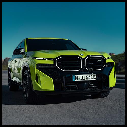 Die Frontansicht des BMW XM 50e zeigt die beleuchtete „Iconic Glow“ Niere, die geteilten Scheinwerfereinheiten und die expressiven Formen der Frontschürze in Hochglanzschwarz.
