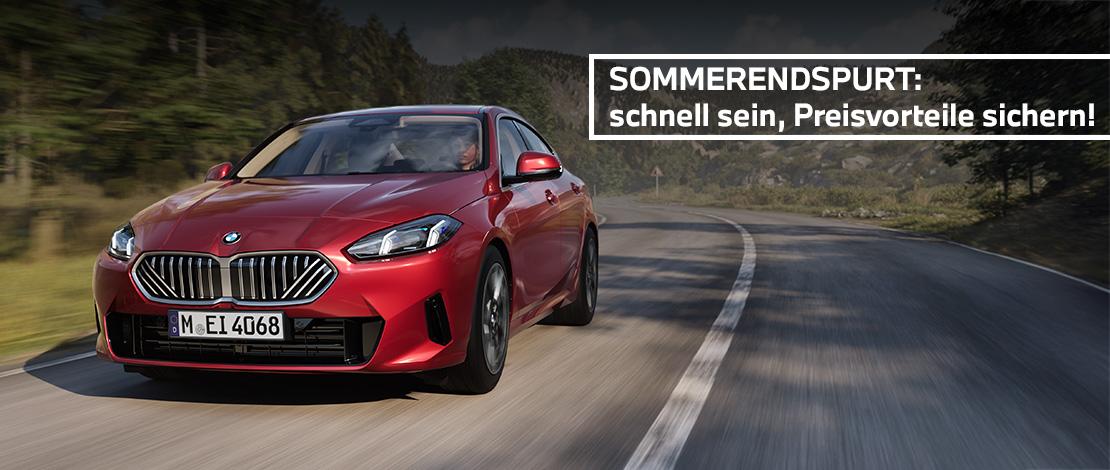 Das Bild zeigt einen roten, viertürigen BMW 2er-Reihe Gran Coupé, der auf einer kurvigen Landstraße fährt. Oben rechts im Bild ist ein weißes Textfeld mit schwarzer Schrift zu sehen, das den Text "SOMMERENDSPURT: schnell sein, Preisvorteile sichern!" enthält. Der Hintergrund ist eine bergige Landschaft mit Bäumen unter einem teilweise dunklen Himmel. Das Kennzeichen "M EI 4068" ist auf der vorderen Stoßstange zu sehen.