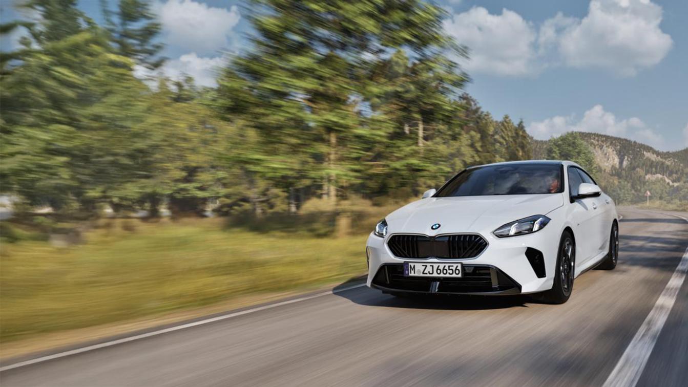 Ein weißes BMW 216 Gran Coupé fährt auf einer kurvigen Straße, die durch eine Wald- und Berglandschaft führt. Das Auto ist leicht von vorne und rechts zu sehen und nimmt den größten Teil der linken Bildhälfte ein. Am unteren Rand des Bildes befindet sich ein Textfeld, das folgende technische Daten enthält: WLTP Energieverbrauch kombiniert: 5,9 l/100km; WLTP CO₂-Emissionen kombiniert: 134 g/km; CO₂-Klasse: D; Leistung: 90 kW (122 PS); Hubraum: 1.499 cm³; Kraftstoff: Benzin. Der Text endet mit dem Hinweis, dass die Abbildung Sonderausstattungen zeigt. Das Kennzeichen des Wagens lautet "M ZJ 6656".