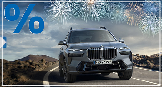 In dieser professionellen Werbegrafik fährt ein dunkelgrauer BMW X7 SUV dynamisch auf einer kurvigen Landstraße durch eine karge, felsige Hügellandschaft direkt auf den Betrachter zu. Über dem Fahrzeug erstrahlen am bewölkten Himmel festliche Feuerwerksgarben in Blau und Gold, während oben links ein großes, blaues Prozentzeichen in 3D-Optik unübersehbar auf ein Sonderangebot zum Jahresstart hinweist. Das gesamte Bild ist in kühlen Grau- und Blautönen gehalten, wirkt durch die Kombination aus Luxusauto und Feuerwerk jedoch sehr feierlich, kraftvoll und exklusiv.